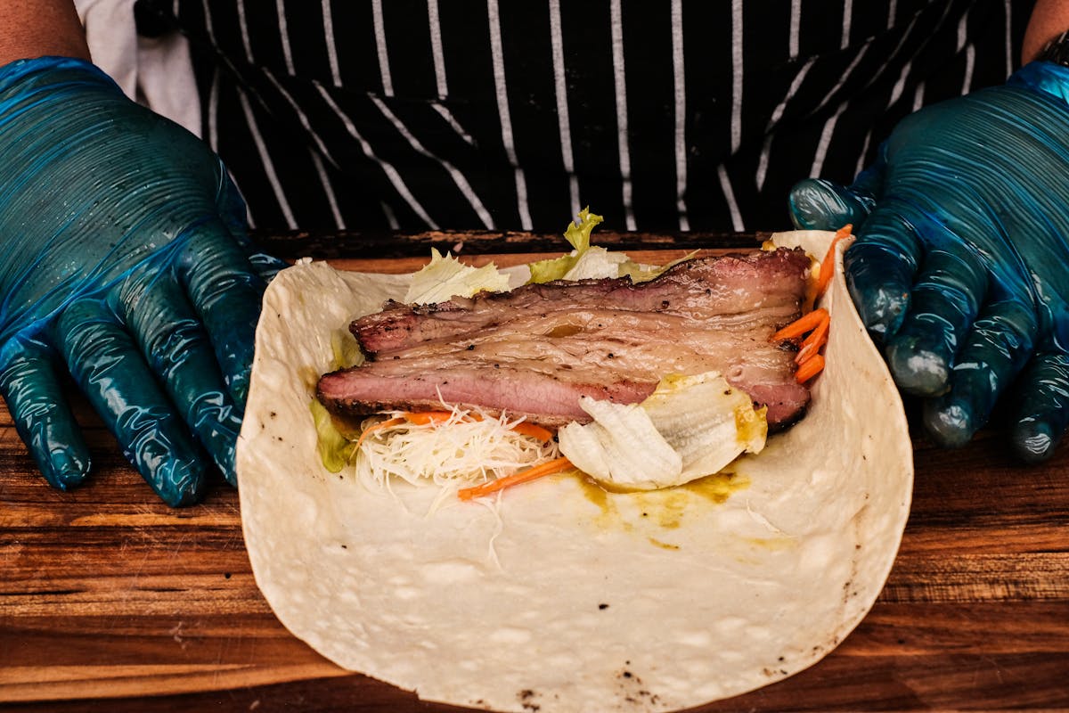 A chef in gloves preparing a wrapped beef bundle, the classic butcher paper or foil wrap step for smoked brisket